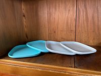 Four vintage Tupperware square plates, two blue and two grey, placed on a wooden surface.