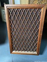 Full front view showing rectangular vintage speaker with wooden lattice diamond pattern over fabric grille, wood frame around edges.
