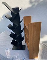 Two bookshelves side by side, one black angular metal bookshelf and one brown wood-finished bookshelf.