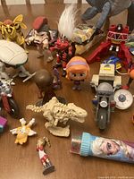 Wide view of assortment including various character figures, dinosaur toys, and a small female figure with orange hair, showing details of paint and sculpting
