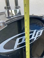 Close-up image of black PDP bass kick drum with tape measure indicating size and visible drum hardware.