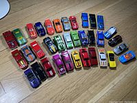 Top view of 32 assorted diecast cars in various colors arranged on a wooden floor.