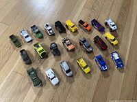 Top view showing all 22 diecast toy trucks in various colors and styles arranged on wooden floor.