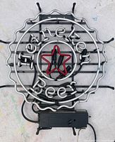Photo of circular Heineken neon sign with red star and silver neon tubing, includes transformer at the bottom