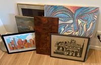 Five framed art works arranged against a wall showing varied styles and colors.