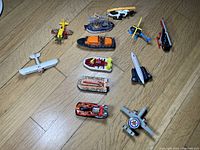 Full lot display with 12 diecast vehicles including boats, planes, and helicopters on wooden floor