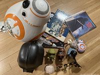 Overview photo showing a large BB-8 figure, Darth Vader helmet, books, DVDs, and multiple Star Wars figurines and toys arranged on floor.