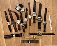 Overall lot of 15 assorted watches laid out on wooden floor, showing various styles and strap types