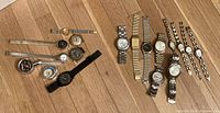 Overview of 14 total watches and timepieces laid out on floor, displaying variety of styles and bands.