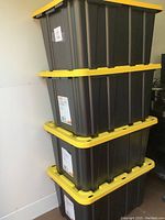 Stack of four HDX Tough Totes with black bodies and yellow lids, showing full lot of four 102 litre capacity storage bins.
