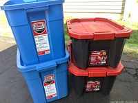 Stack of two Rubbermaid Roughneck blue totes next to two black Husky 15-gallon latch and stack totes with red lids.