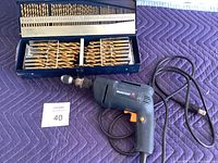 Mastercraft corded electric drill placed next to a metal case containing multiple sizes of drill bits.
