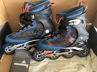 Photo showing pair of black, blue, and orange K2 X-Training inline rollerblades in original box with skate manual.