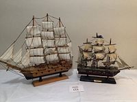 Both wooden model sailboats placed on white surface showing size difference and detailed sails and rigging.