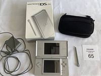 Top view of the Nintendo DS Lite handheld console open, charger, carrying case, stylus, and original box on a white surface.