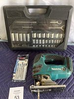 Photo of Job Mate socket set in black carrying case with clear top with sockets and wrench inside, Makita LXT cordless jigsaw, and Bosch jigsaw blades package on a blue padded surface.