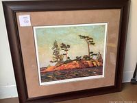 Framed artwork with a scenic impressionistic landscape of rocks and trees by water.