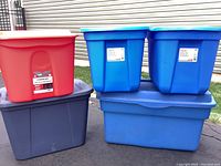 Six plastic storage totes in various sizes and colors stacked outside against a garage door.