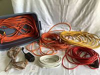 Overview of all extension cords laid out with some coiled inside a gray plastic tote.