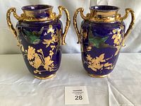Front side of both vases showing gold floral patterns and bird motifs on cobalt blue background with gold handles.