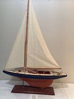 Front-left side view of the wooden sailboat sculpture with white linen sails and wooden stand.