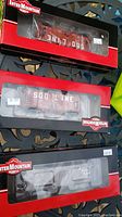 Three InterMountain model train cars in unopened packaging, two red SOO LINE boxcars and one black enclosed car.