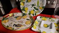 Full view of three pieces: a round serving tray, a square dip dish, and an oval platter, all decorated with lemons, leaves, and script detailing.