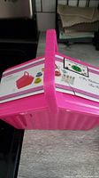 Side view of bright pink plastic carry case for tea set on table with handle upright