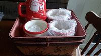 Top-down view showing a red Santa mug with 'Got Milk and Cookies' text, two white Santa mugs with red trim wrapped in protective foam inside a decorated wooden basket.