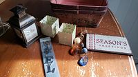 Photo showing the full lot including the black metal lantern, white tea light holders, vintage wooden baskets, Seasons Greetings sign, metal Noel sign, and yule jewel ornaments