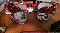 Two glass Cardinal candle holders featuring red stained glass cardinals with pine cone and pine needle decorations, shown from top angle on wooden surface.