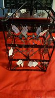 Photo of earrings hanging on metal display stand showing various styles including hoops, leaf designs, and charm earrings with price tags.