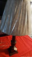 Full view of the table lamp showing wood base and fabric lampshade covered in plastic