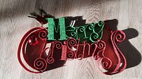 Photo of the full glitter Merry Christmas metal sign in red and green with decorative swirling accents.