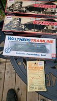 Photo of two Atlas Trainman HO Scale train cars boxed, one Walthers Trainline boxed train car, and Walthers Magne-Matic model adapter kit on an outdoor table.