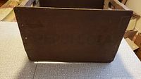 Side view of wooden crate showing stamped Pepsi Cola branding faintly visible on dark brown wood.