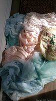 Multiple pastel-colored vintage robes and nighties laid out, showing pink, blue, and cream silk fabrics with lace and embroidery details.