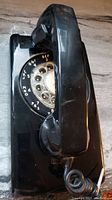 Side angle showing black rotary dial phone with handset hanging on cradle, coiled cord visible