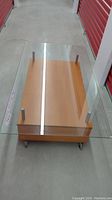 Top view of coffee table showing clear glass top with wooden base underneath and caster wheels