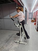 Side view showing person using the step glider fitness machine in a hallway with metal walls and concrete floor.