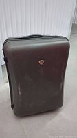 Dark brown hard cover suitcase standing upright on floor with visible scuff marks.