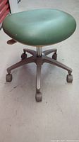 Front view of the office stool showing mint green seat and metal base with caster wheels.