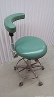Front view of the green dental stool showing round vinyl seat, curved half-moon armrest, and base with casters