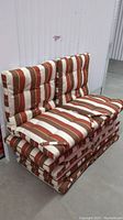 Stack of 6 outdoor cushions, showing front and sides with striped rust orange and beige pattern and strap attachments