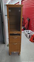 Tall cabinet from front showing frosted glass door, four drawers, and wood legs.