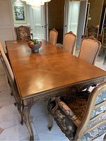 Photo taken showing the side view of the large wooden dining table, highlighting the ornate carved legs and trim as well as the parquet tabletop pattern.