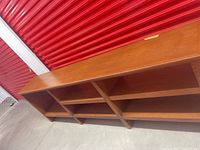 Full length view of the walnut bookshelf showing five shelves in six compartments, against a red storage door.