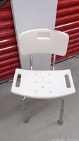 Front view of white waterproof shower support chair showing textured backrest, handles, and metal legs with rubber tips.