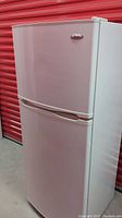 Full front view of the white Whirlpool top freezer refrigerator showing slight pinkish reflection and integrated handle.