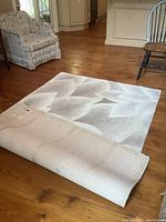 View of the area rug partially rolled to show texture, color, and pattern.